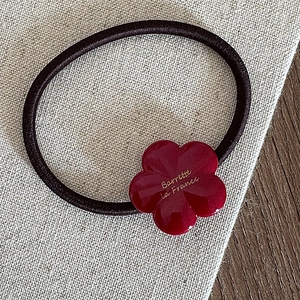 Gros plan d'un chouchou élastique avec un pendentif fleur en acétate rouge sur lin