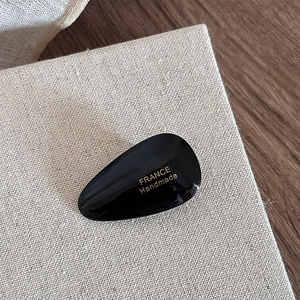 Detailed macro view of black acetate water drop hair clip with golden handmade logo