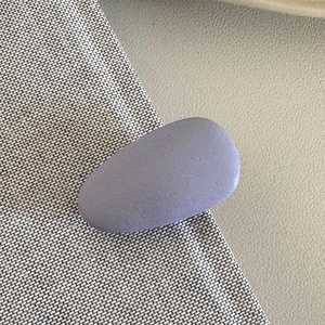 Close-up of matte purple oval hair clip with fine sandy texture on leather background