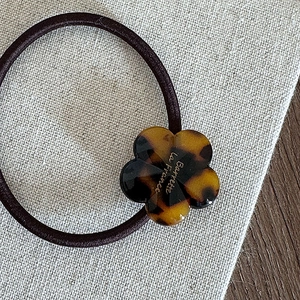Détail d'une fleur en acétate écaillé avec gravure dorée sur un élastique à cheveux