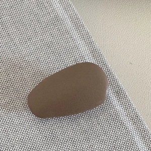 Close-up of matte brown drop-shaped leather hair clip on beige woven fabric
