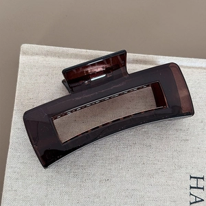 Close-up of translucent dark brown hair claw clip with a glossy finish on beige linen