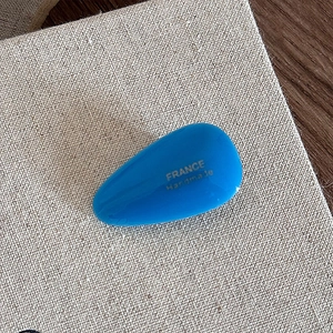Macro detail of glossy blue acetate teardrop hair clip with golden France Handmade logo