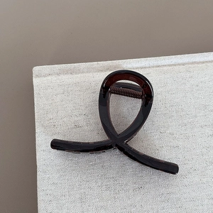 Detail view of the brown resin hair claw clip with crossed loop design on linen texture