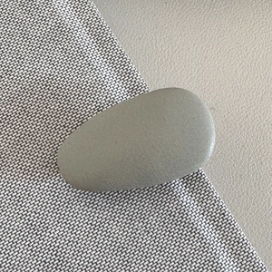 Detail of matte cream droplet hair clip showing smooth texture on woven and leather background