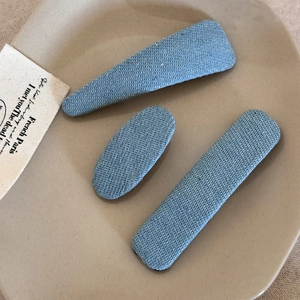 Three vintage denim fabric hair clips in geometric shapes on a beige ceramic plate