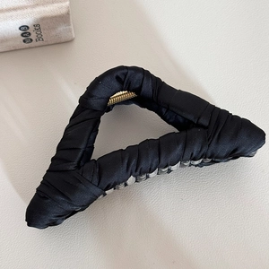 Detail view of large black satin hair claw clip with golden spring on leather background