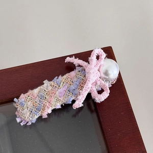 Detail einer Tweed-Haarspange mit gewebter Schleife und großer Perle auf Holzrahmen