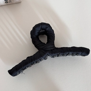 Macro detail of black fabric-wrapped hair claw clip showing pleated satin texture