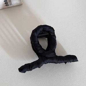 Detail view of black satin fabric wrapped hair claw clip on cream textured leather surface