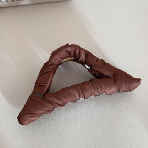 Detail of elegant dark brown pleated satin fabric wrapped on a large metal shark hair claw