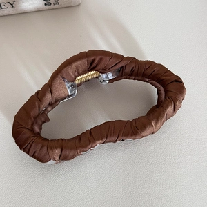 Detailed top view of brown satin fabric wrapped shark hair claw on leather background