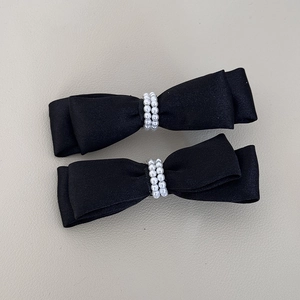 Detail of two black satin bow hair clips featuring double rows of white faux pearls