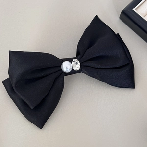 Detailed view of black satin bow hair clip with faux pearl and rhinestone centerpiece