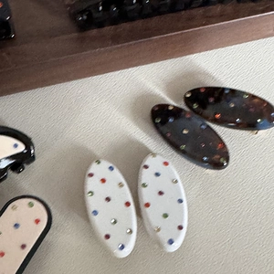 Dettaglio di fermagli per capelli in acetato con strass colorati su fondo strutturato