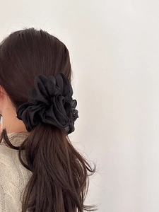 Detailed view of a black ruffled organza scrunchie tied on long hair in a ponytail
