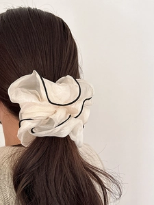 Detailed view of an oversized cream organza scrunchie with black trim on brown hair