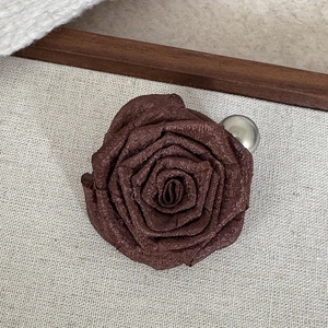 Close-up of a brown fabric rose hair clip with textured petals and a silver metallic ball