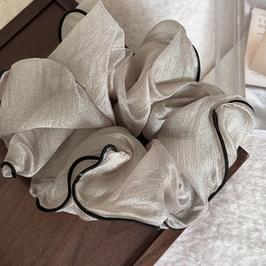 Close-up of champagne gold organza scrunchie with contrasting black hem on a wooden tray