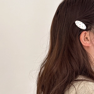 Dettaglio di un fermaglio ovale bianco con strass colorati su capelli castani mossi