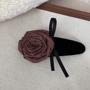 Detailed view of dark brown silk rose hair clip with black ribbon on cream canvas
