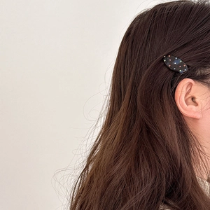 Primo piano di una molletta in acetato nero con strass colorati sui capelli castani