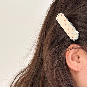 Dettaglio molletta per capelli color crema con strass colorati su capelli scuri