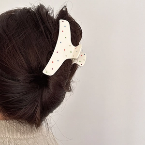 Dettaglio di una pinza per capelli in acetato crema con strass colorati sui capelli