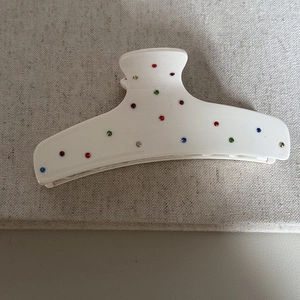 Dettaglio di un fermaglio per capelli bianco con strass colorati su sfondo di lino