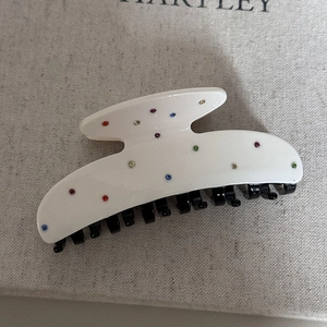 Vista dettagliata di una clip per capelli in acetato bianco con strass colorati incastonati