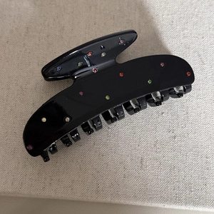 Dettaglio di un grande fermaglio nero per capelli con strass colorati e finitura lucida