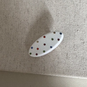 Dettaglio della pinza per capelli in acetato panna con strass colorati su tessuto