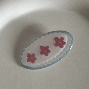 Détail de la barrette ovale bleue à bords ondulés avec motifs de fleurs roses
