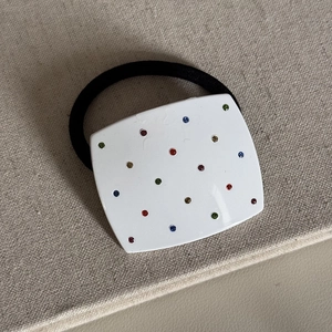 Dettaglio di elastico per capelli in acetato bianco con strass colorati e fascia nera