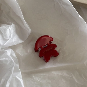 Dettaglio di una mini clip per capelli rosso scuro su carta bianca con logo dorato