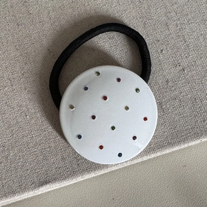 Dettaglio di un fermaglio per capelli in acetato bianco con strass colorati su tela