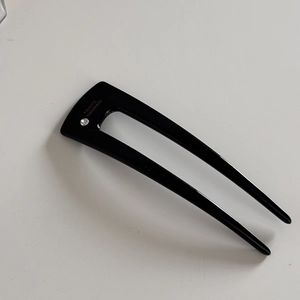 Close-up of sleek black U-shaped hair pin with rhinestone detail and handmade lettering