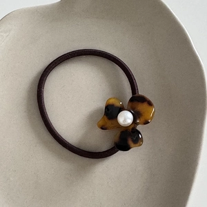 Detailed view of acetate flower hair tie with tortoiseshell texture and pearl center