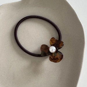 Detail of flower hair tie featuring tortoise shell resin petals and a white faux pearl
