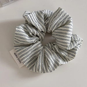 Detail of blue striped seersucker scrunchie with handmade paper tag on white surface