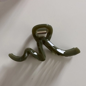 Detailed view of large olive green hair claw clip with wavy resin design and gold spring