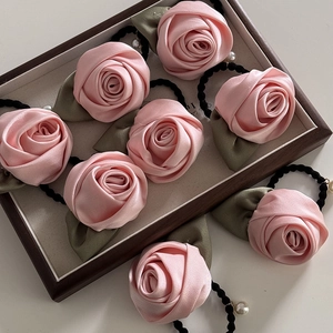 Gros plan de chouchous roses en satin en forme de rose avec feuilles vertes et perles blanches