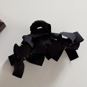 Dettaglio dei fiocchi in raso nero multistrato su una pinza per capelli minimalista