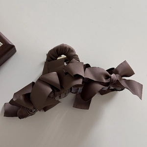 Dettaglio del fermaglio per capelli in raso marrone caffè con fiocco plissettato