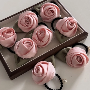 Chouchou fleur rose satinée avec feuilles vertes et pendentif perle sur plateau en bois