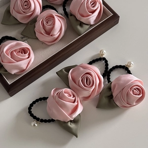 Détail du chouchou rose en satin avec feuilles vertes et une perle blanche suspendue