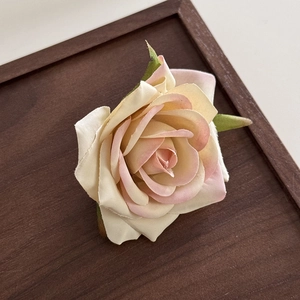Macro detail of gradient cream pink fabric rose hair clip with realistic green leaves decoration