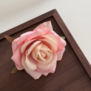 Close-up of pink fabric misty rose flower clip with layered petals and green leaves decoration