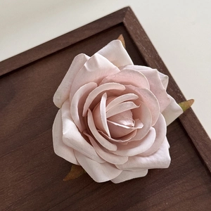 Detailed macro view of a pink fabric rose hair clip on a vintage wooden tray