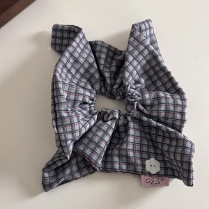 Detail of plaid scrunchie with a white flower button and pink label on fabric